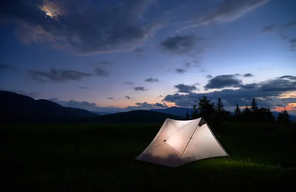 Calm campsite beside a still lake at dusk with soft mountain silhouettes